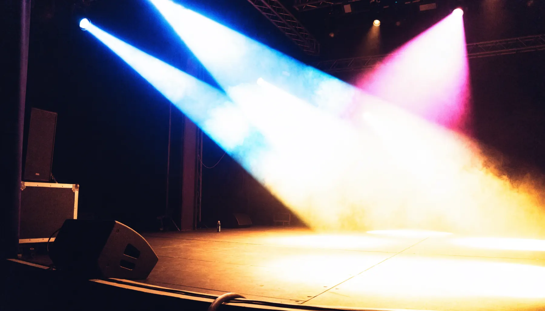 An empty stage at night, cyan and magenta beams cutting through the haze